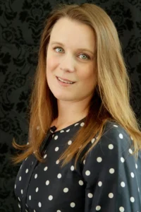 A woman with long hair and polka dots is smiling.